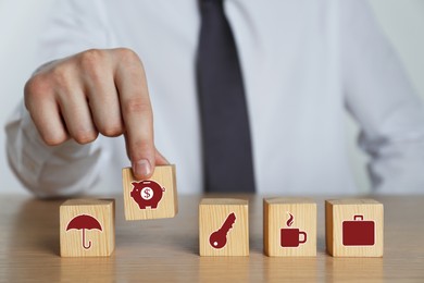 Man and wooden cubes with different icons on wooden table, closeup. Insurance concept