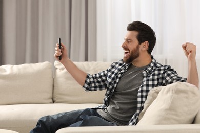 Photo of Excited man watching TV on sofa at home