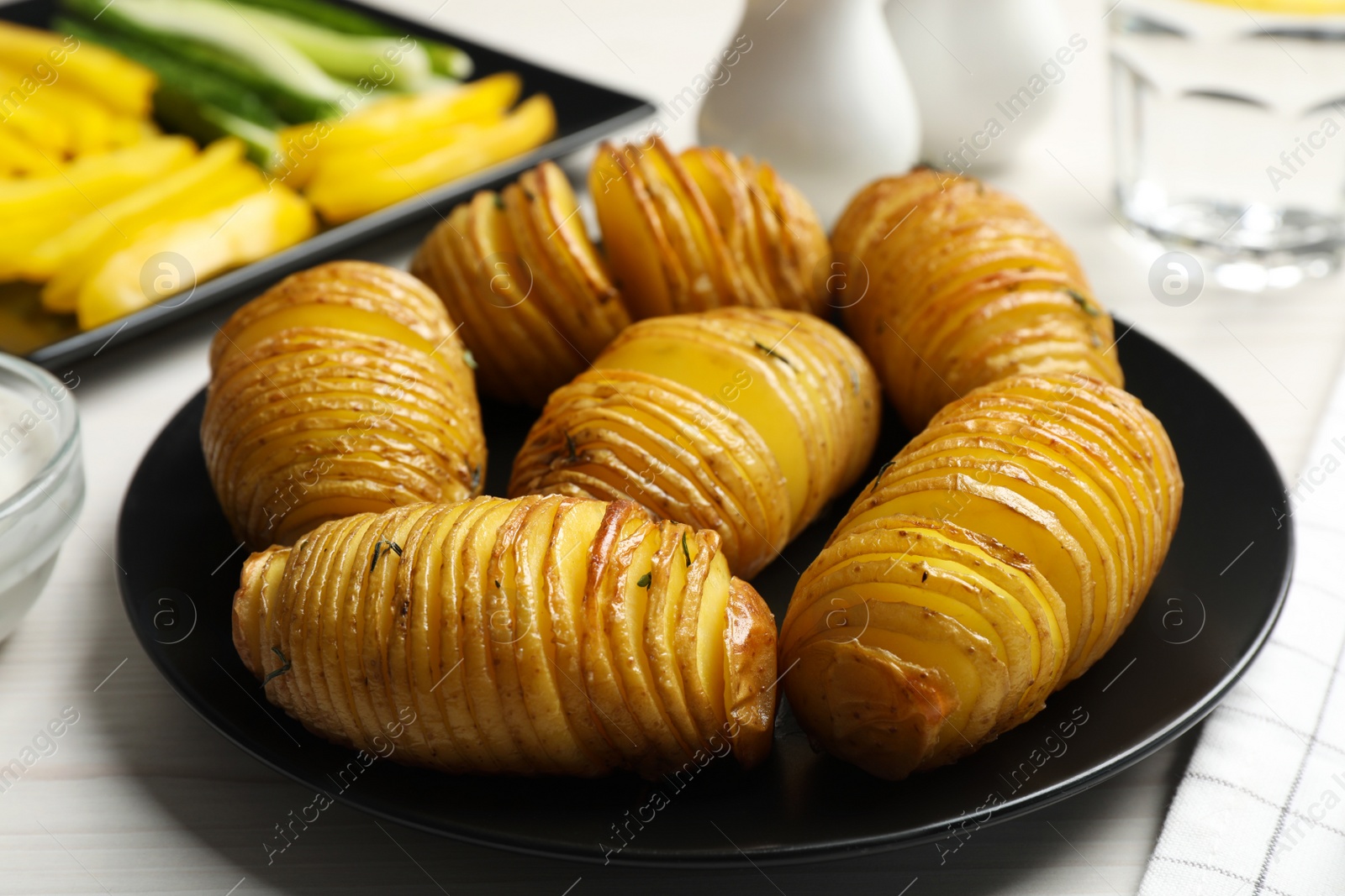 Photo of Delicious homemade Hasselback potatoes served on white wooden table, closeup