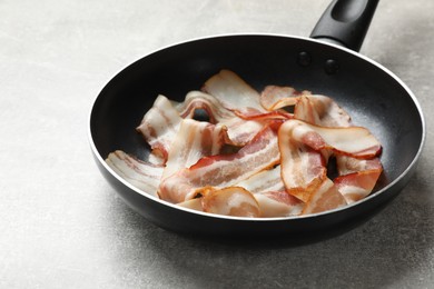 Photo of Delicious bacon slices in frying pan on light grey table