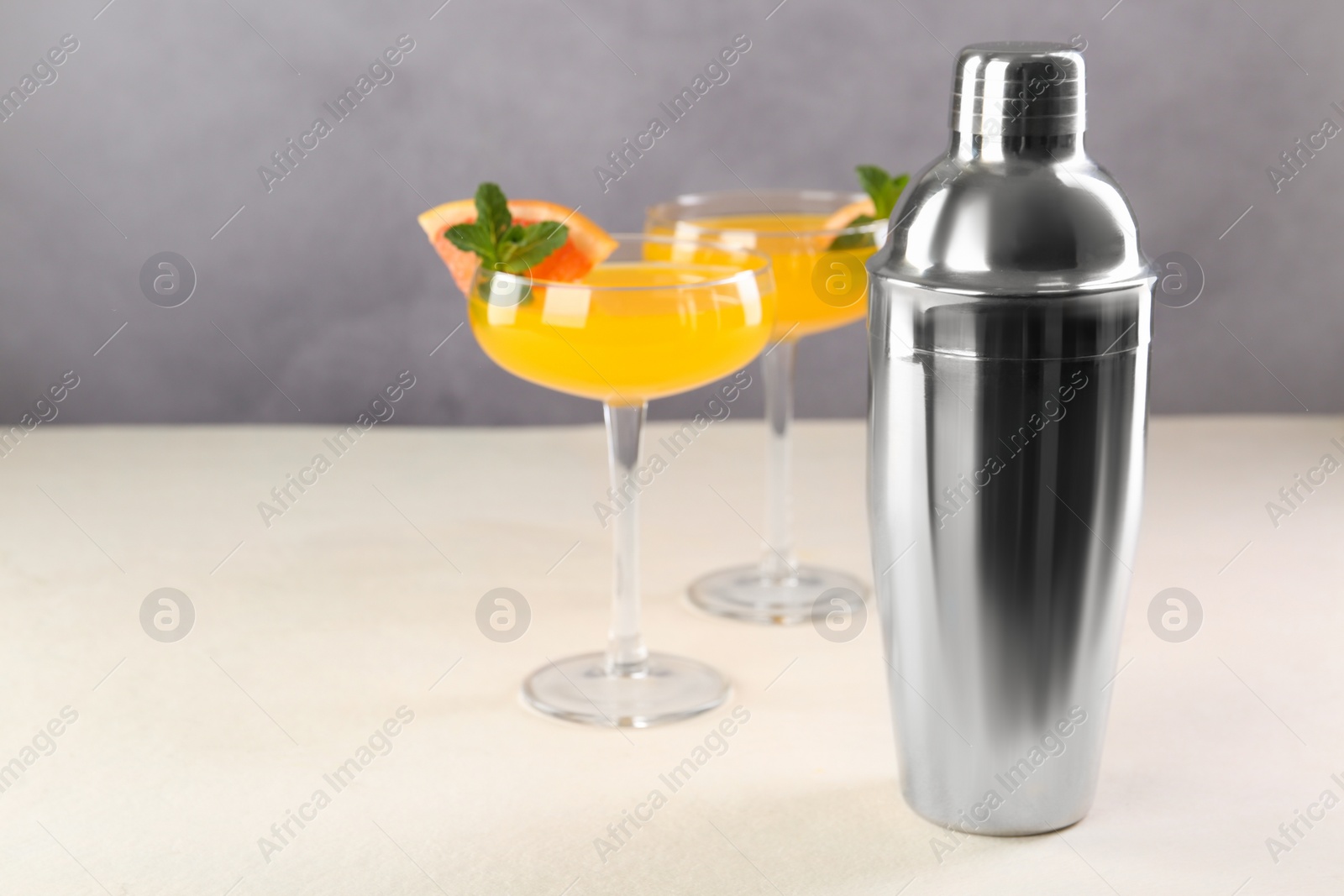 Photo of Metal shaker and delicious cocktails on light table, space for text