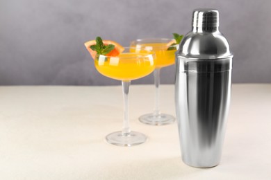 Photo of Metal shaker and delicious cocktails on light table, space for text