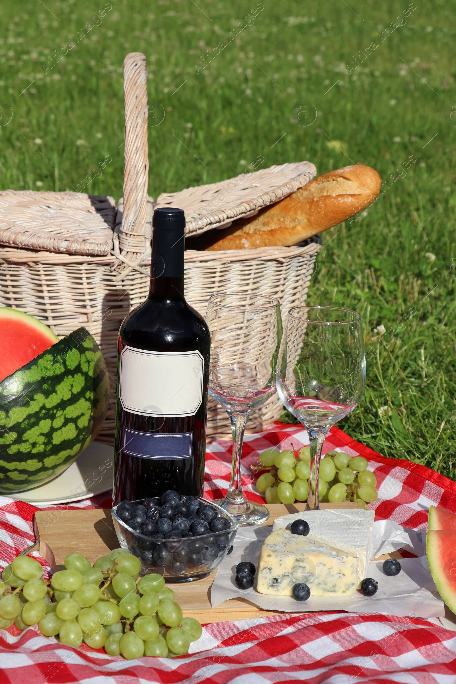 Photo of Picnic blanket with delicious food and wine outdoors on summer day