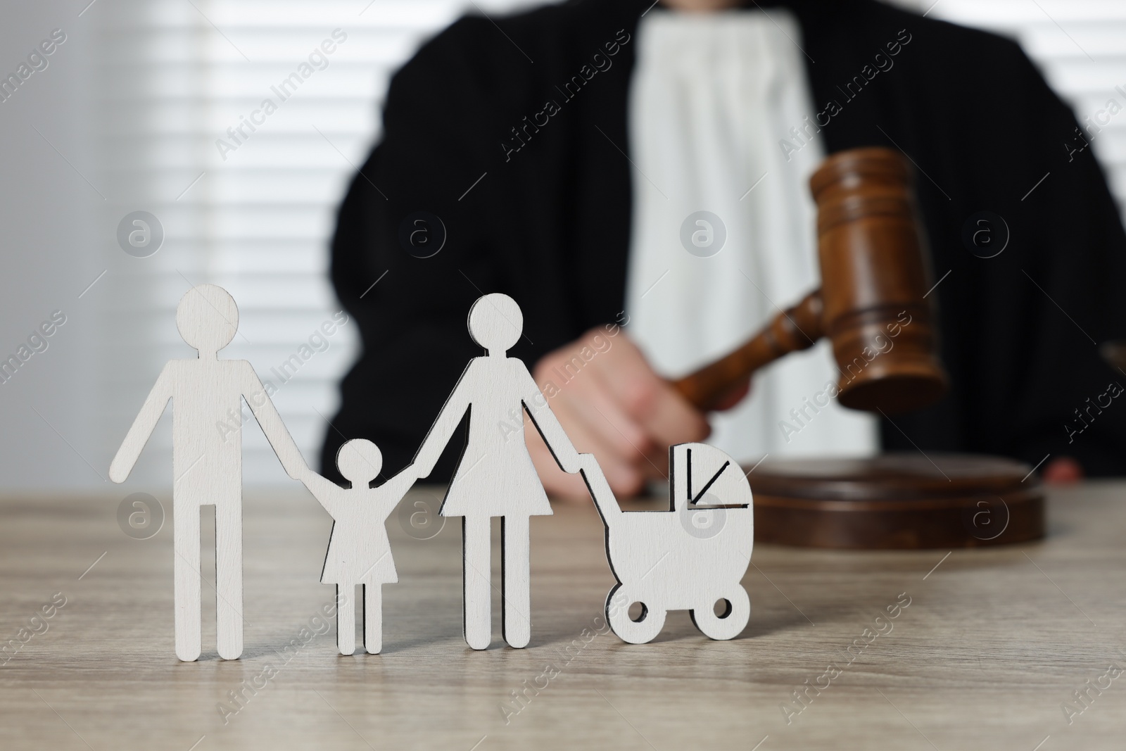 Photo of Family law. Judge with gavel sitting at wooden table, focus on figure of parents and children