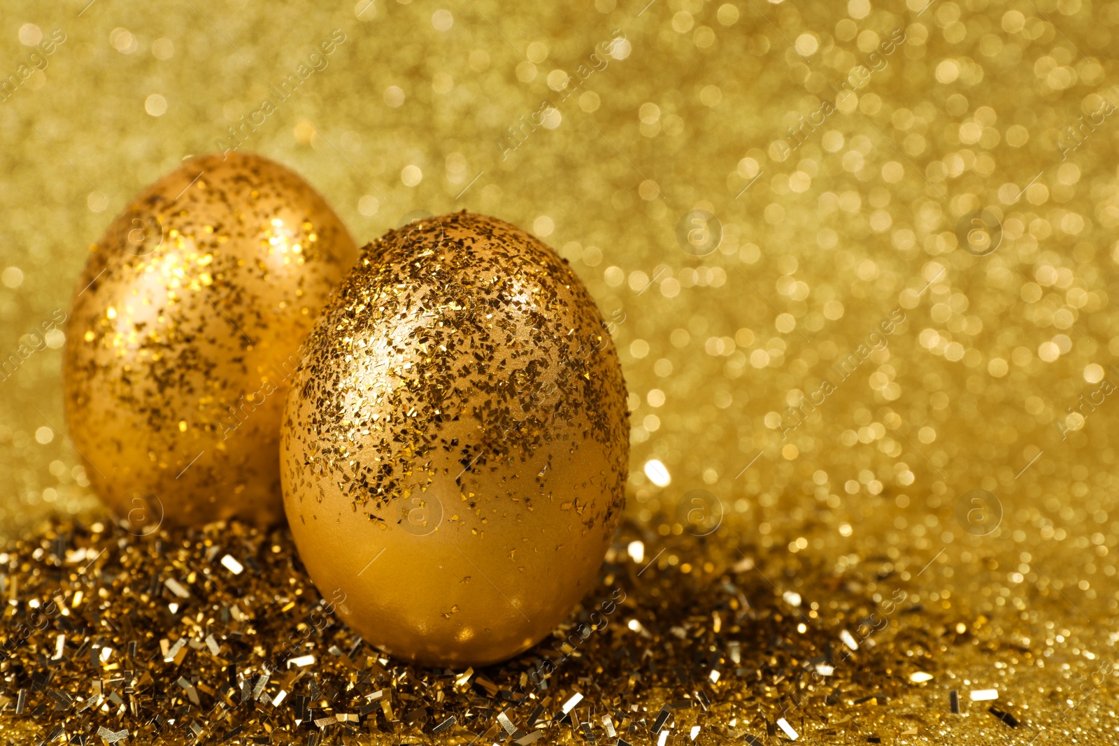 Photo of Shiny golden eggs with glitter on yellow background, closeup. Space for text
