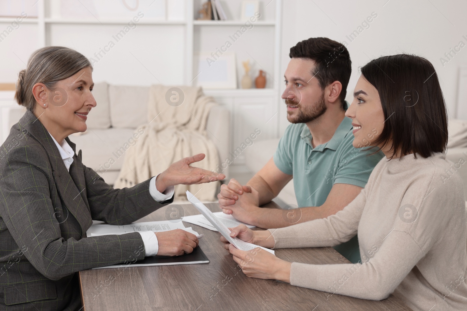 Photo of Young couple consulting insurance agent about pension plan at wooden table indoors