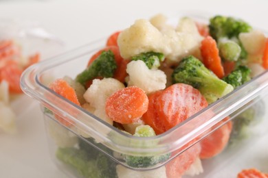 Mix of different frozen vegetables in plastic container on white table, closeup