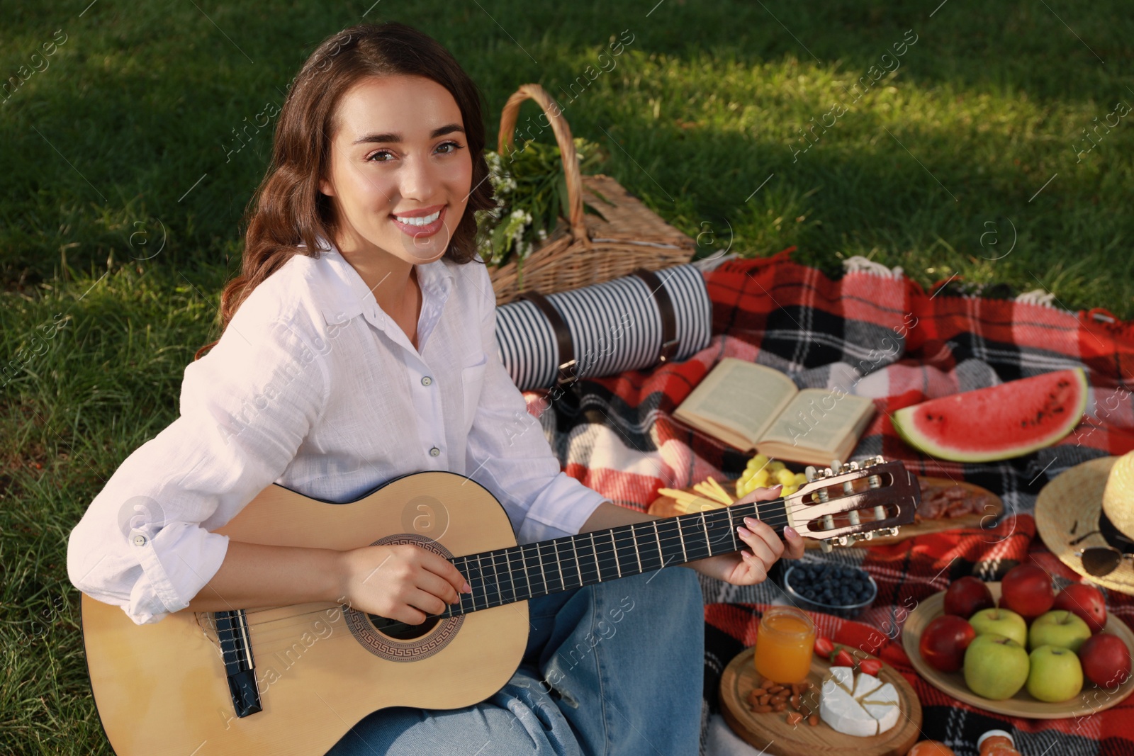 Photo of Happy young woman with guitar on plaid outdoors. Summer picnic