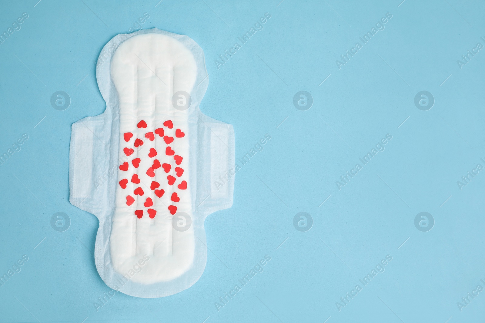 Photo of Menstrual pad with confetti on light blue background, top view. Space for text