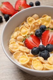 Photo of Delicious crispy cornflakes with milk and fresh berries on wooden table, closeup
