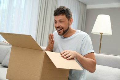 Photo of Happy man opening parcel on sofa at home. Internet shopping