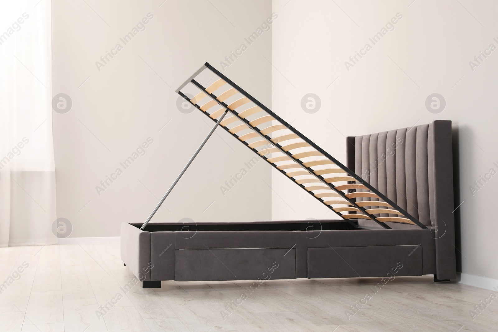 Photo of Comfortable bed with storage space for bedding under lifted slatted base in room