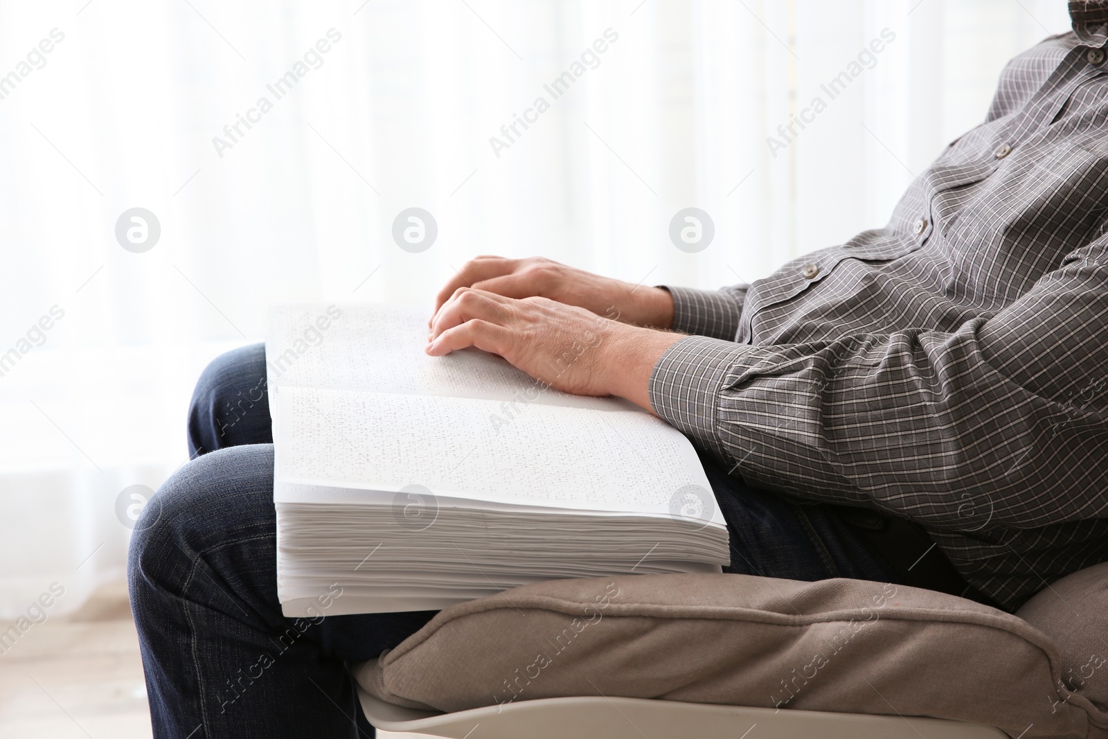 Photo of Blind man reading book written in Braille at home, closeup