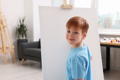 Photo of Little boy painting in studio. Using easel to hold canvas