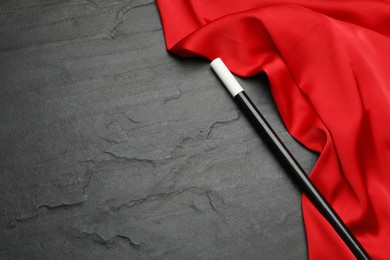 Photo of Beautiful magic wand and red fabric on black table, top view. Space for text