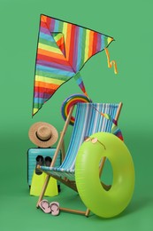 Photo of Deck chair, kite, suitcase and beach accessories on green background. Summer vacation
