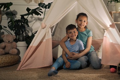 Cute little children in toy wigwam at home