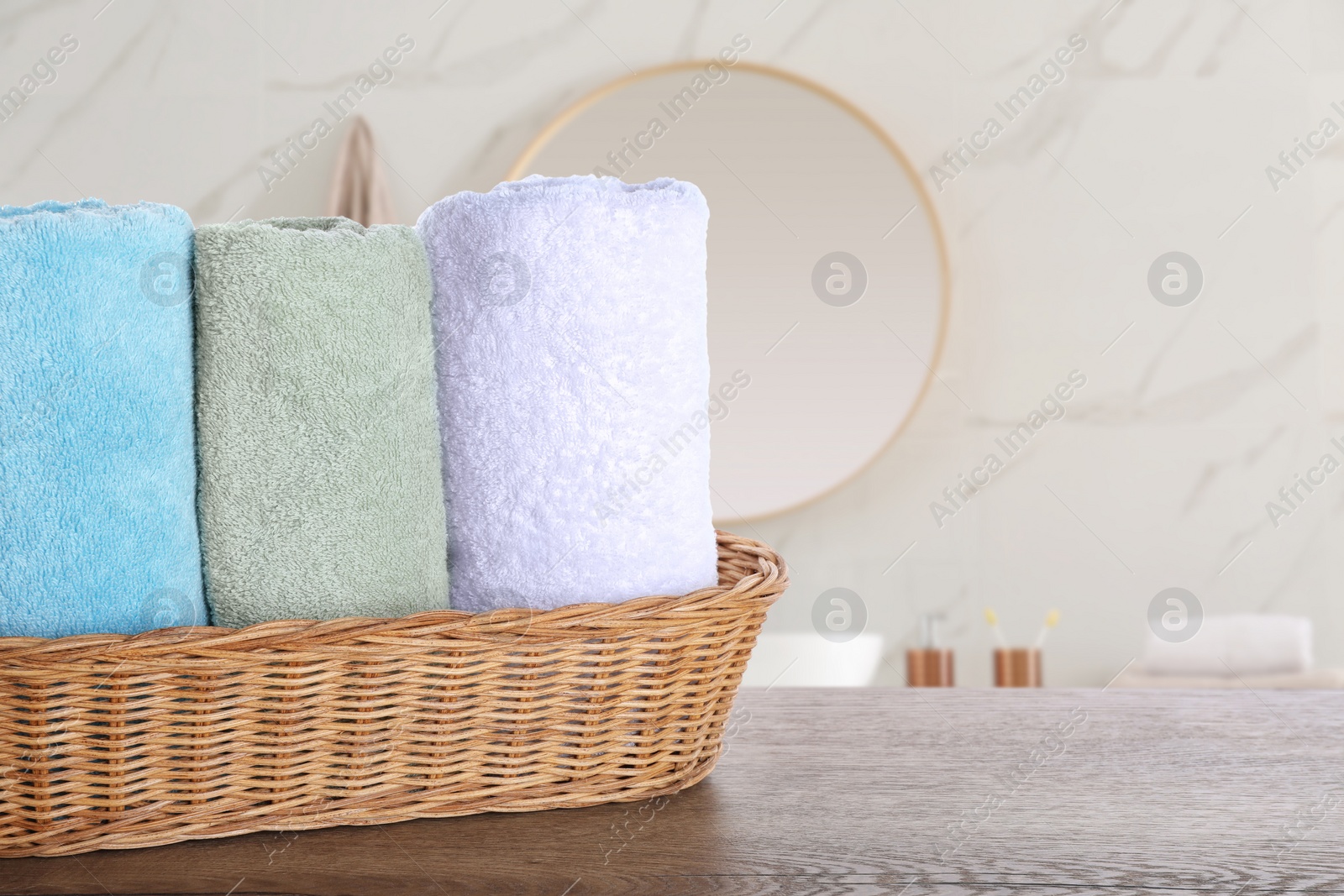 Image of Wicker basket with clean soft towels on wooden table in bathroom. Space for text