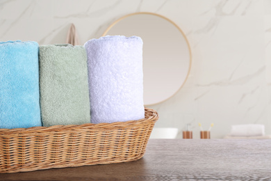 Image of Wicker basket with clean soft towels on wooden table in bathroom. Space for text