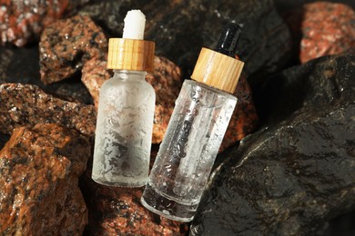 Photo of Bottles of face serum on wet stones, closeup