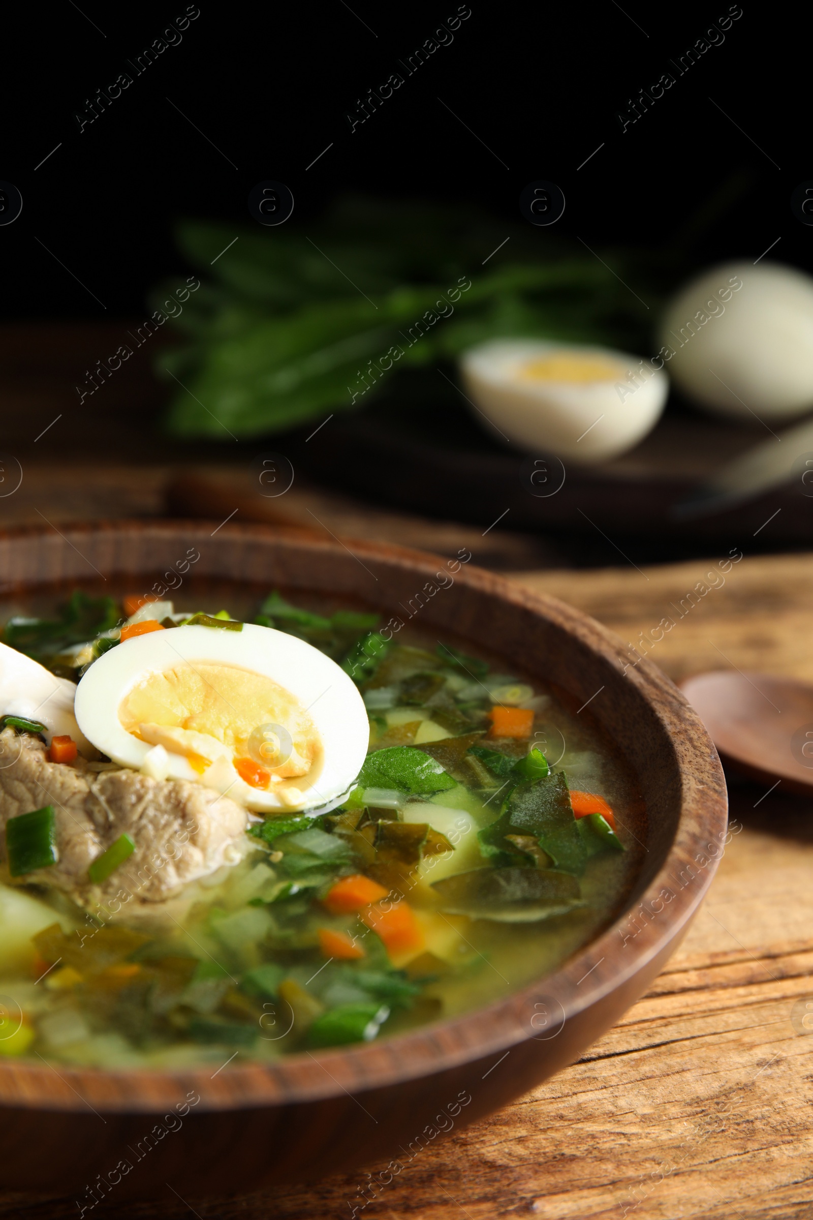Photo of Delicious sorrel soup with meat and egg served on  wooden table, closeup