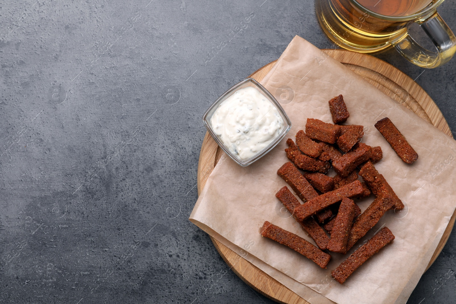 Photo of Crispy rusks served with beer and dip sauce on grey table, flat lay. Space for text