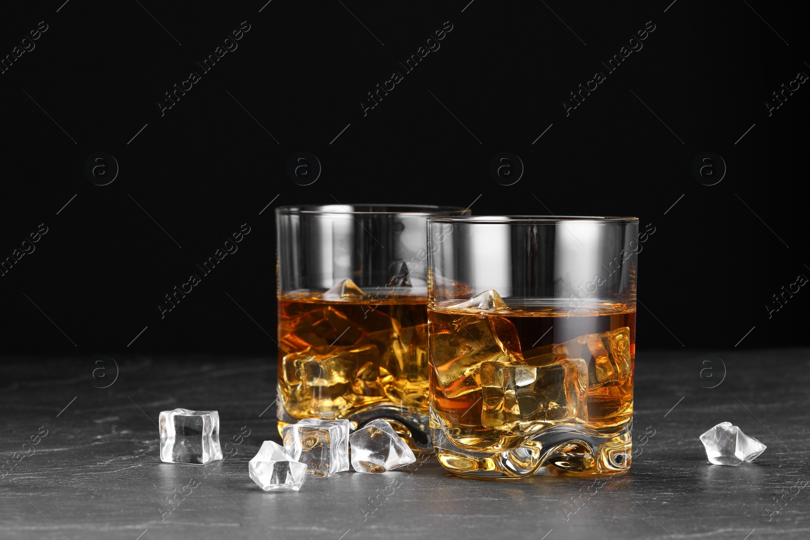 Photo of Whiskey and ice cubes in glasses on black table, closeup