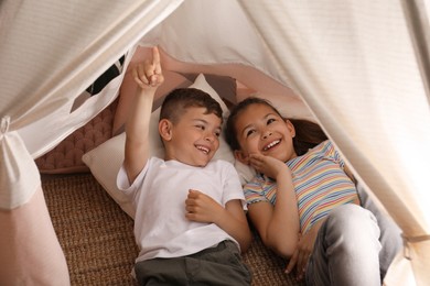 Photo of Cute little children lying in toy wigwam at home