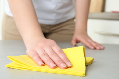 Photo of Woman wiping grey table with rag indoors, closeup