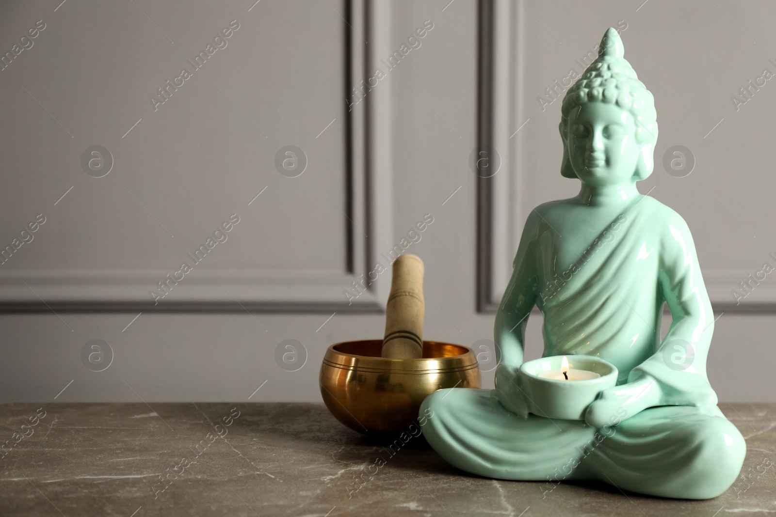 Photo of Buddha statue with burning candle near singing bowl on grey table. Space for text