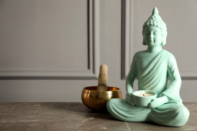Photo of Buddha statue with burning candle near singing bowl on grey table. Space for text