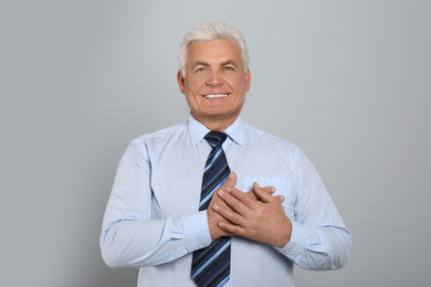 Photo of Grateful senior man with hands on chest against light grey background