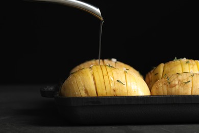 Photo of Oiling raw Hasselback potatoes before baking on dark grey table, closeup