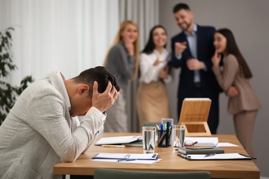 Photo of Coworkers bullying their colleague at workplace in office, space for text