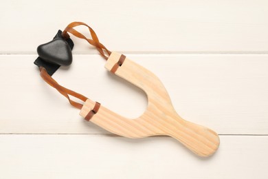 Slingshot with pebble on white wooden background, top view