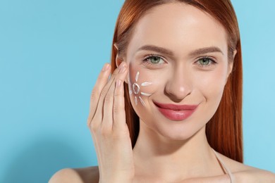Beautiful young woman with sun protection cream on her face against light blue background, space for text