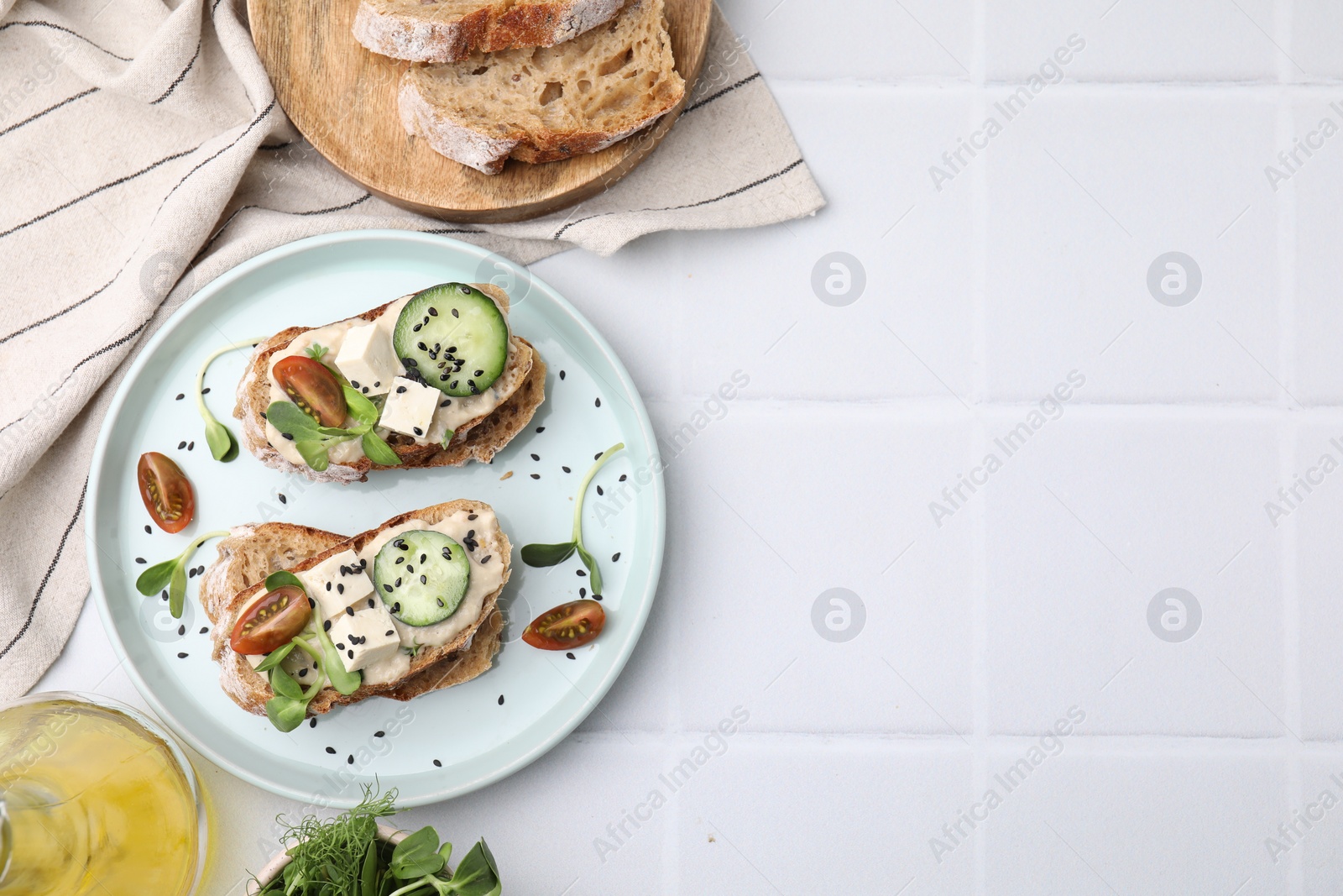 Photo of Tasty vegan sandwiches with tofu, cucumber, tomato and sesame seeds on white tiled table, flat lay. Space for text