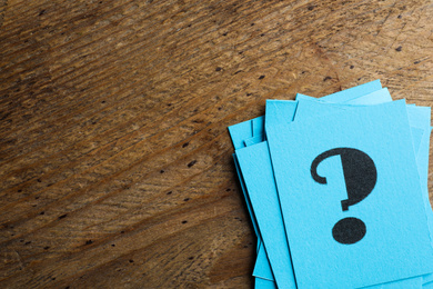 Blue paper cards with question mark on wooden background, top view. Space for text