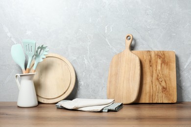 Wooden cutting boards and utensils on table near gray wall