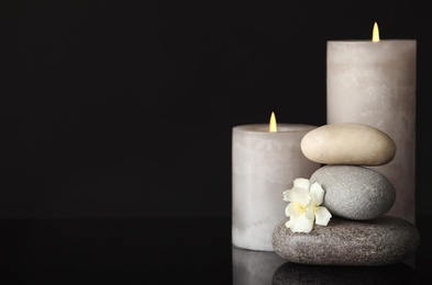 Photo of Stack of spa stones, burning candles and fresh flower on black background. Space for text