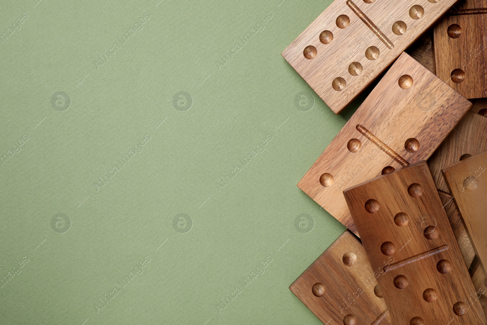 Photo of Wooden domino tiles on green background, flat lay. Space for text