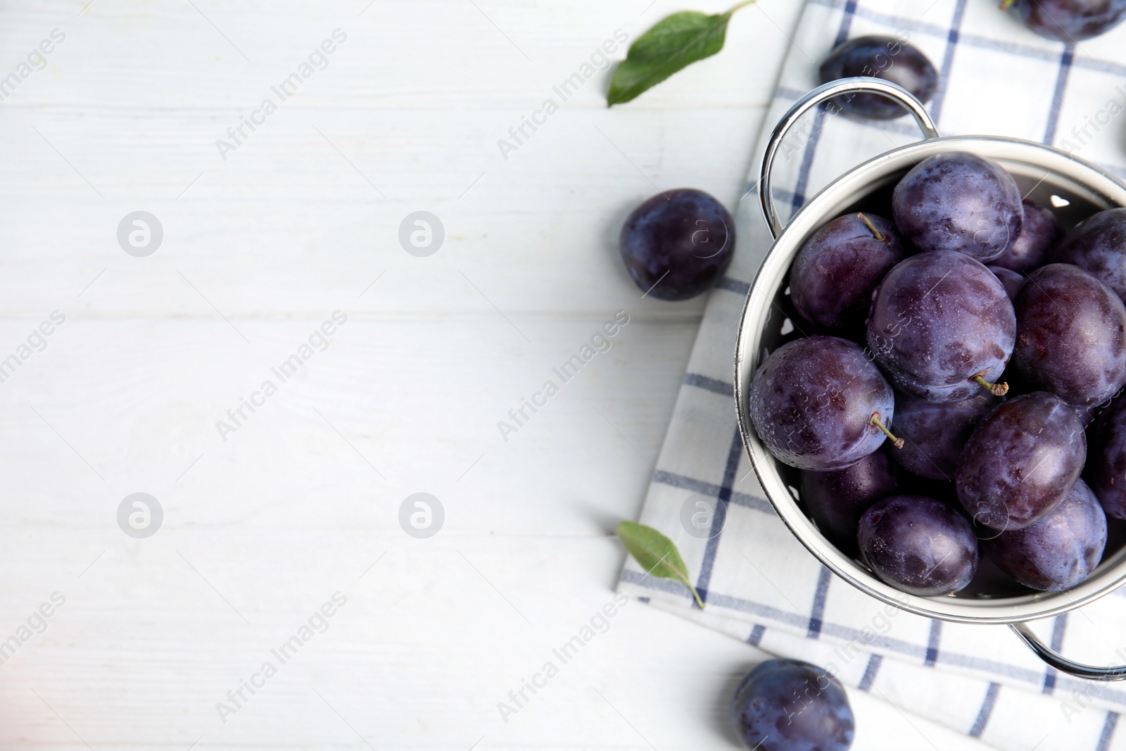 Photo of Delicious ripe plums in colander on white table, flat lay. Space for text