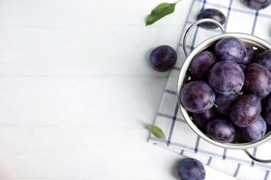 Delicious ripe plums in colander on white table, flat lay. Space for text