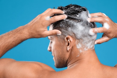 Handsome man washing hair on light blue background, back view