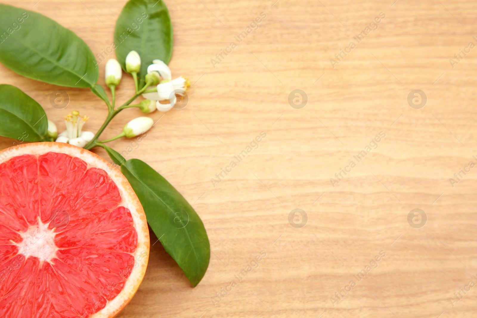 Photo of Cut fresh ripe grapefruit and green leaves on wooden table, above view. Space for text