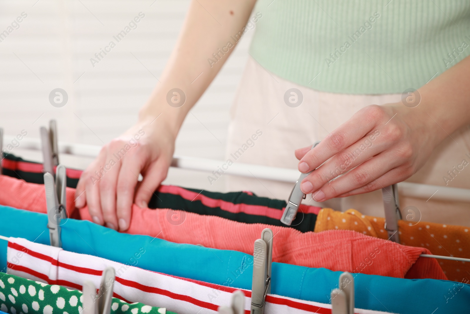 Photo of Woman hanging clean laundry on drying rack indoors, closeup