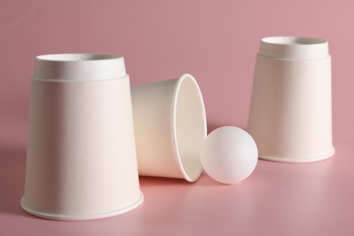 Shell game. Three paper cups and ball on pink background