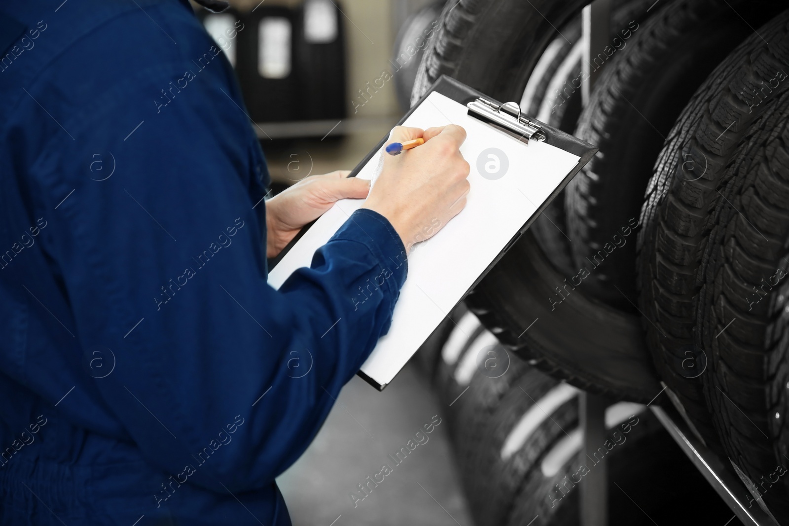 Photo of Young male mechanic with clipboard near tires in automobile service center