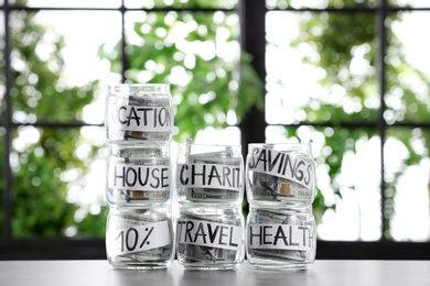 Glass jars with money for different needs on table against blurred background