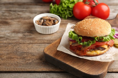 Photo of Tasty burger with bacon on wooden board. Space for text